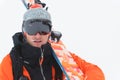 Portrait of a professional athlete skier in an orange jacket wearing a black mask and with skis on his shoulder looks Royalty Free Stock Photo