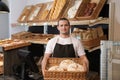 Portrait of professional baker holding tray with fresh bread near showcase