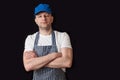 Portrait of a professional butcher in black and white apron, white t shirt and blue baseball hat, armed crossed, looking at the