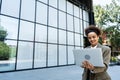 Portrait of professional female financial lawyer standing in front of an office on street communicating online using tablet, Royalty Free Stock Photo