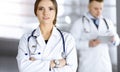 Portrait of a professional friendly woman doctor with a stethoscope, standing with crossed arms in a sunny clinic. Young