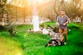 Professional gardener using lawn mower and cutting grass during summer sunset