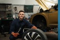 Portrait of professional mechanic with car wheel at automobile repair shop Royalty Free Stock Photo
