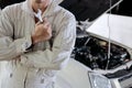 Portrait of professional young mechanic man in uniform holding wrench against car in open hood at the repair garage. Royalty Free Stock Photo