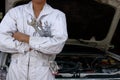 Portrait of professional young mechanic man in uniform holding wrench against car in open hood at the repair garage. Royalty Free Stock Photo