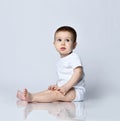 Portrait in profile of calm newborn baby boy toddler sitting sideways on the floor looking at us on a gray Royalty Free Stock Photo