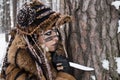 Portrait of a hunter`s girl in fur clothes, which holds a knife stuck in the bark of a pine