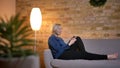 Portrait in profile of senior caucasian lady on sofa watching into smartphone with modest smile in cozy home atmosphere.