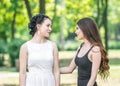 Portrait in profile of two young beautiful women friends talking in green summer park. Pretty females Bride and bridesmaid smiling Royalty Free Stock Photo