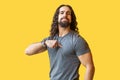 Portrait of proud bearded young man with long curly hair in grey tshirt standing, pointing himself and looking at camera with Royalty Free Stock Photo