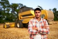 Portrait of proud harvester machine driver with hands crossed on chest. Farmer standing at his combine. Agronomist