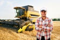 Portrait of proud harvester machine driver with hands crossed on chest. Farmer standing at his combine. Agronomist