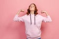 Portrait of proud young female in hoodie showing biceps, expressing power ambitions to become successful, female rights, feminism