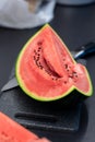 A portrait of a quarter slice of a green cut watermelon lying on a plastic cutting board next to a knife. The piece of the fruit