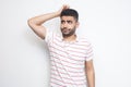 Portrait of query handsome bearded young man in striped t-shirt standing scratching his head, planing and thinking about something Royalty Free Stock Photo