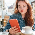 Portrait of red curled long hair caucasian teen girl sitting on a cozy cafe outdoor terrace on the street using the modern Royalty Free Stock Photo