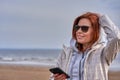 Portrait of a red-haired middle-aged woman in sunglasses and a raincoat looking at a smartphone. Sunny spring morning Royalty Free Stock Photo