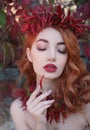 Portrait of a red-haired sexy woman with red full lips in a crown and a necklace of hot chili peppers with a pepper in Royalty Free Stock Photo