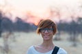 Portrait of a red haired woman with green eyes, eyeglasses and smiling facial expression. Sunset at the horizon. Shot outdoors wit Royalty Free Stock Photo