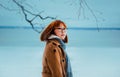 Portrait of a red-haired young Asian woman in a beige coat, who walks near the frozen sea in winter in the park. Travel in the Royalty Free Stock Photo