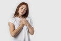 Portrait of a red-haired young woman keeps hands on chest, expresses sympathy. Kind hearted friendly nice girl shows kindness,