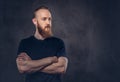 Portrait of a redhead bearded man dressed in a black t-shirt standing with crossed arms. Isolated on a dark textured