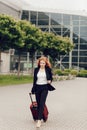 Portrait of a redhead businesswoman in black formal suit with red luggage going for business travel trip. Royalty Free Stock Photo