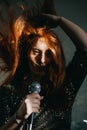 Portrait of redhead female singer woman in sparkly evening dress holding microphone. Singer at microphone. Woman singing Royalty Free Stock Photo