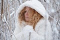 Portrait of redhead, mature woman in her fifties with snowflakes on red curly hair, with hooded coat, freezes in the snowy winter Royalty Free Stock Photo