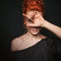 Portrait of redhead woman with blue eyes. Girl looks directly into the camera through her fingers.