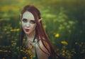 Portrait of a redheaded girl elf in a green swimsuit posing in a clearing of yellow flowers. Fantastic young woman with Royalty Free Stock Photo