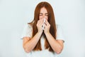 Portrait of redheaded young sick woman suffering from running nose, having flu, blowing her nose standing on  white Royalty Free Stock Photo