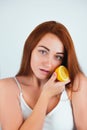 Portrait of redheaded young woman looks sensual standing on isolated white background holding half of orange in hand near her face Royalty Free Stock Photo