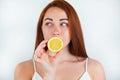 Portrait of redheaded young woman standing on isolated white background holding half of orange in hand near her mouth , beauty Royalty Free Stock Photo