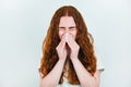 Portrait of redheaded young woman suffering from running nose, having flu, blowing her nose standing on  white backgroung Royalty Free Stock Photo