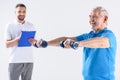 portrait of rehabilitation therapist with notepad assisting senior man exercising with dumbbells Royalty Free Stock Photo