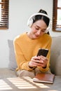 Relaxed Asian woman wearing headphones, listening to music, and using her smartphone Royalty Free Stock Photo