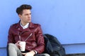 Portrait of a relaxed modern man sitting outdoors with cup of coffee and his backpack Royalty Free Stock Photo