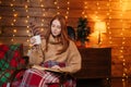 Portrait of relaxed redhead young woman drinking tea and reading book while sitting at cozy armchair Royalty Free Stock Photo