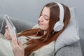 Portrait of relaxed woman with headphone sitting at sofa and listening music on digital tablet. Royalty Free Stock Photo