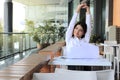 Portrait of relaxed young Asian business woman sitting and raising hands over head in office. Royalty Free Stock Photo