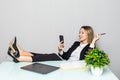 Portrait of a relaxed young businesswoman holding phone sitting with legs on desk in a office Royalty Free Stock Photo
