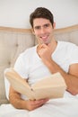 Portrait of relaxed young man reading book in bed Royalty Free Stock Photo