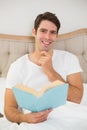 Portrait of relaxed young man reading book in bed Royalty Free Stock Photo