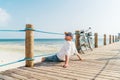 Portrait of relaxing man dressed in light summer clothes and sunglasses sitting and enjoying time and beach view on wooden pier. Royalty Free Stock Photo