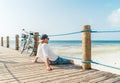 Portrait of relaxing man dressed in light summer clothes and sunglasses sitting and enjoying time and beach view on wooden pier. Royalty Free Stock Photo