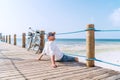 Portrait of relaxing man dressed in light summer clothes and sunglasses sitting and enjoying time and beach view on wooden pier. Royalty Free Stock Photo