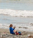 Portrait of relaxing woman sitting on a sand at seaside and taking pictures with her mobile phone Royalty Free Stock Photo