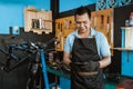 Portrait of a repairman in an apron using a cellphone while repairing a bicycle