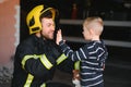 Portrait of rescued little boy with firefighter man standing near fire truck. Firefighter in fire fighting operation.